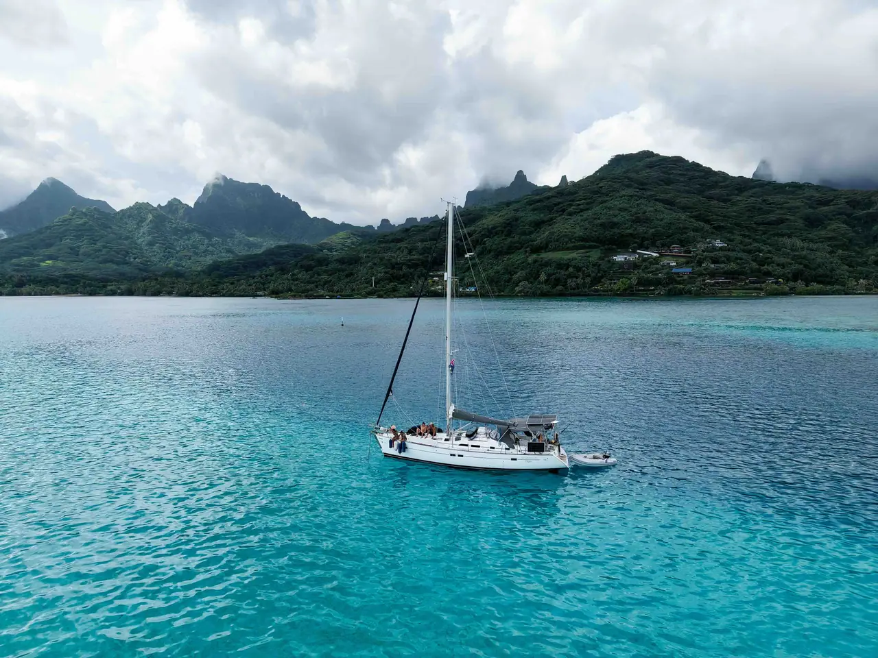 A cruising yacht anchored in clear blue water beneath a mountainous Pacific island